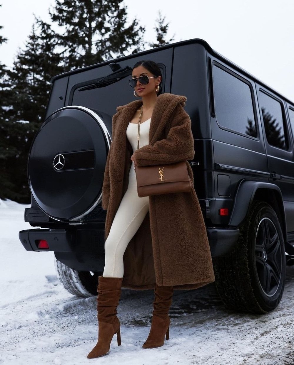 Woman in a teddy coat with a Saint Laurent bag beside a black SUV